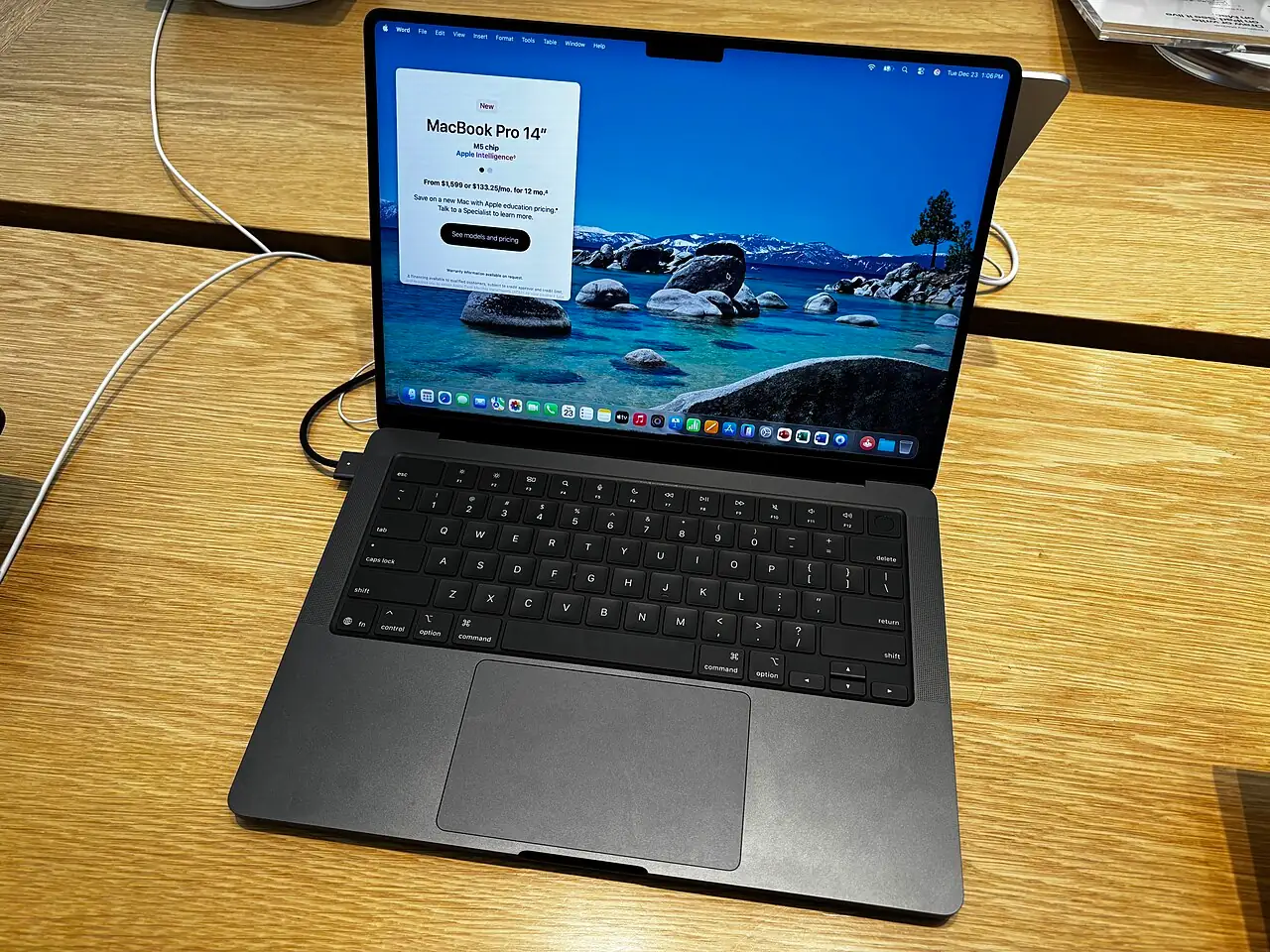 A MacBook Pro 14-inch (M5, Space Black) on a wooden table at an Apple Store.